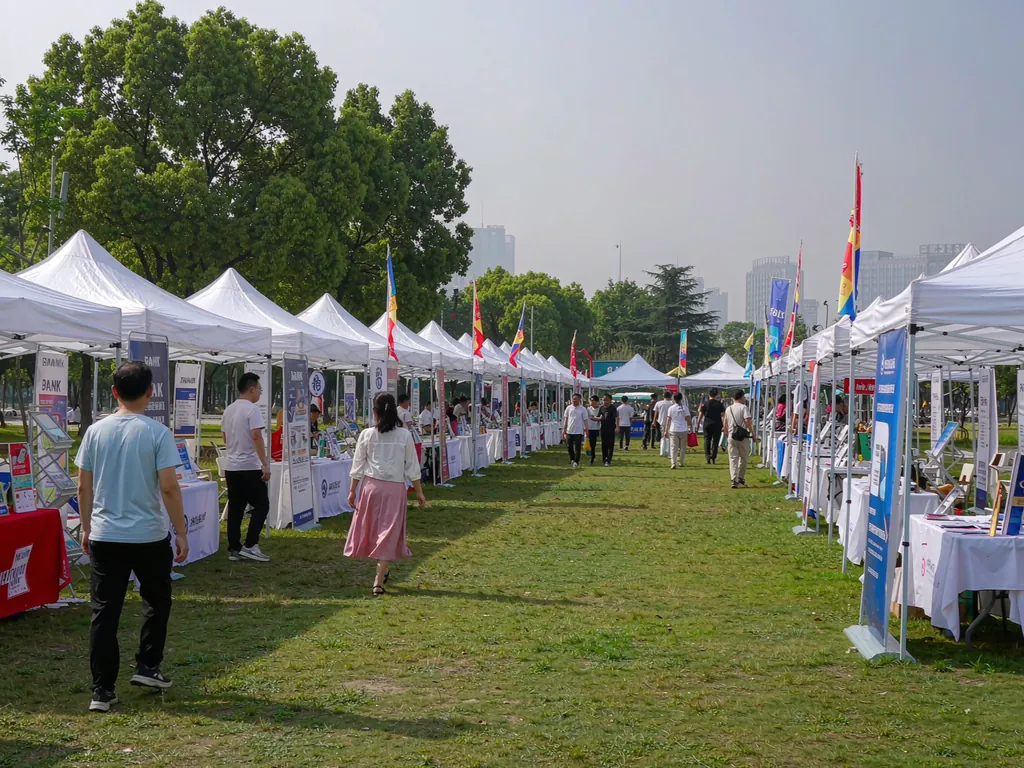 白天公园草坪上的展会帐篷阵列，白色顶棚沿通道排开，有旗帜装饰
